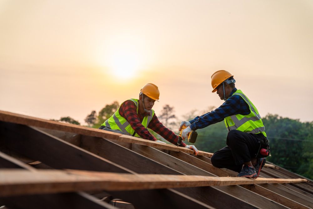 Two construction workers in hard hats securing roof panels at sunrise