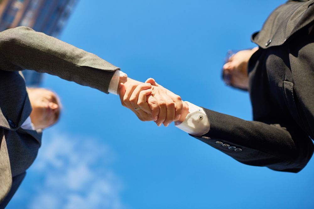 Two businesspeople shaking hands against a blue sky