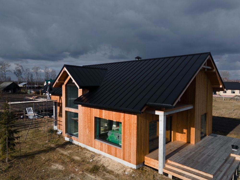 Modern small wooden house with a black metal roof and deck under a cloudy sky