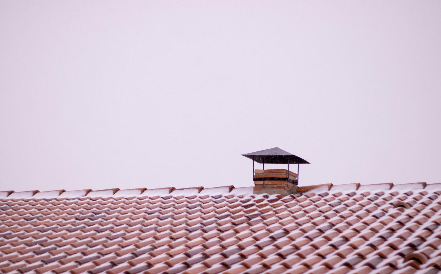 Snow-dusted red tiled roof with a small chimney under a pale sky