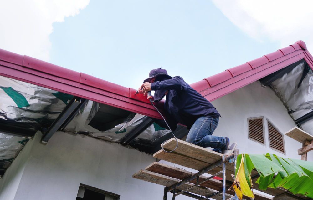 Worker repairing a red roof from a scaffold on a house with banana plants nearby