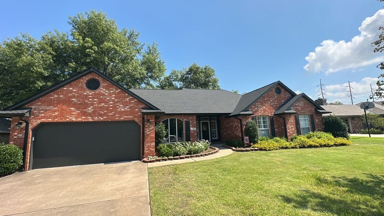Single-story brick house with black garage door, green lawn, and blue sky