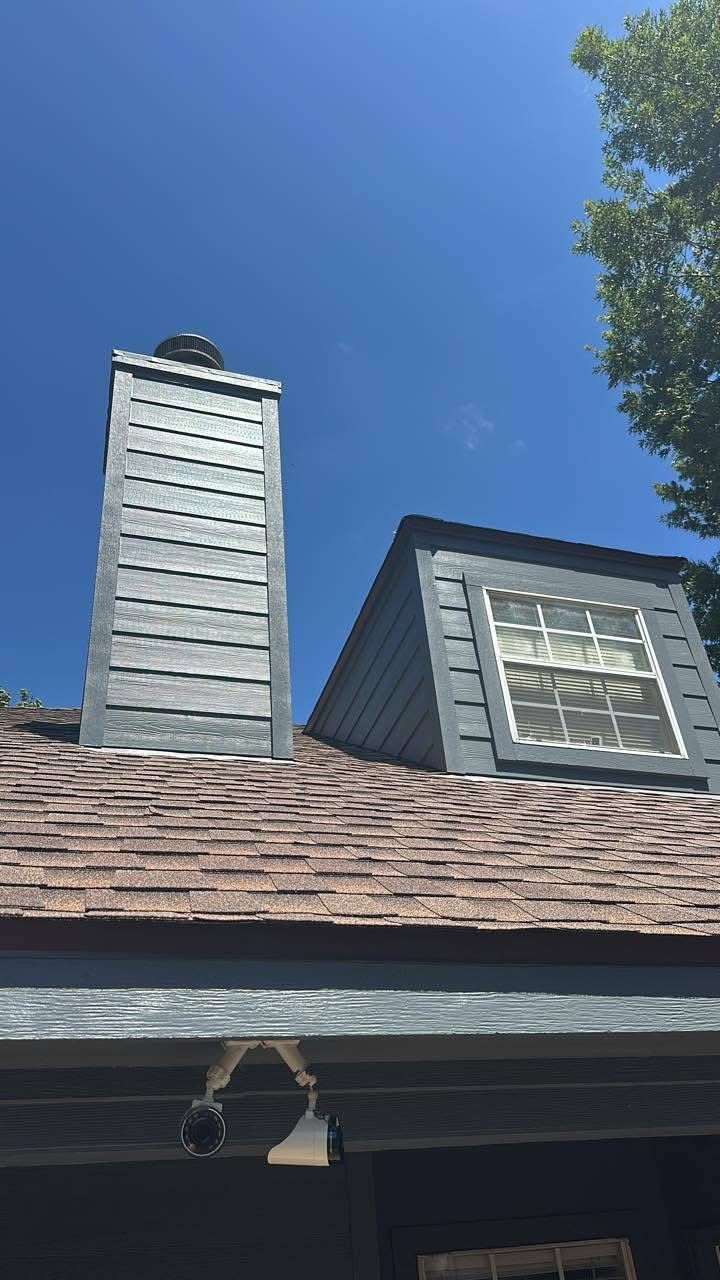 Gray house roof with two chimneys and a small dormer against a clear blue sky