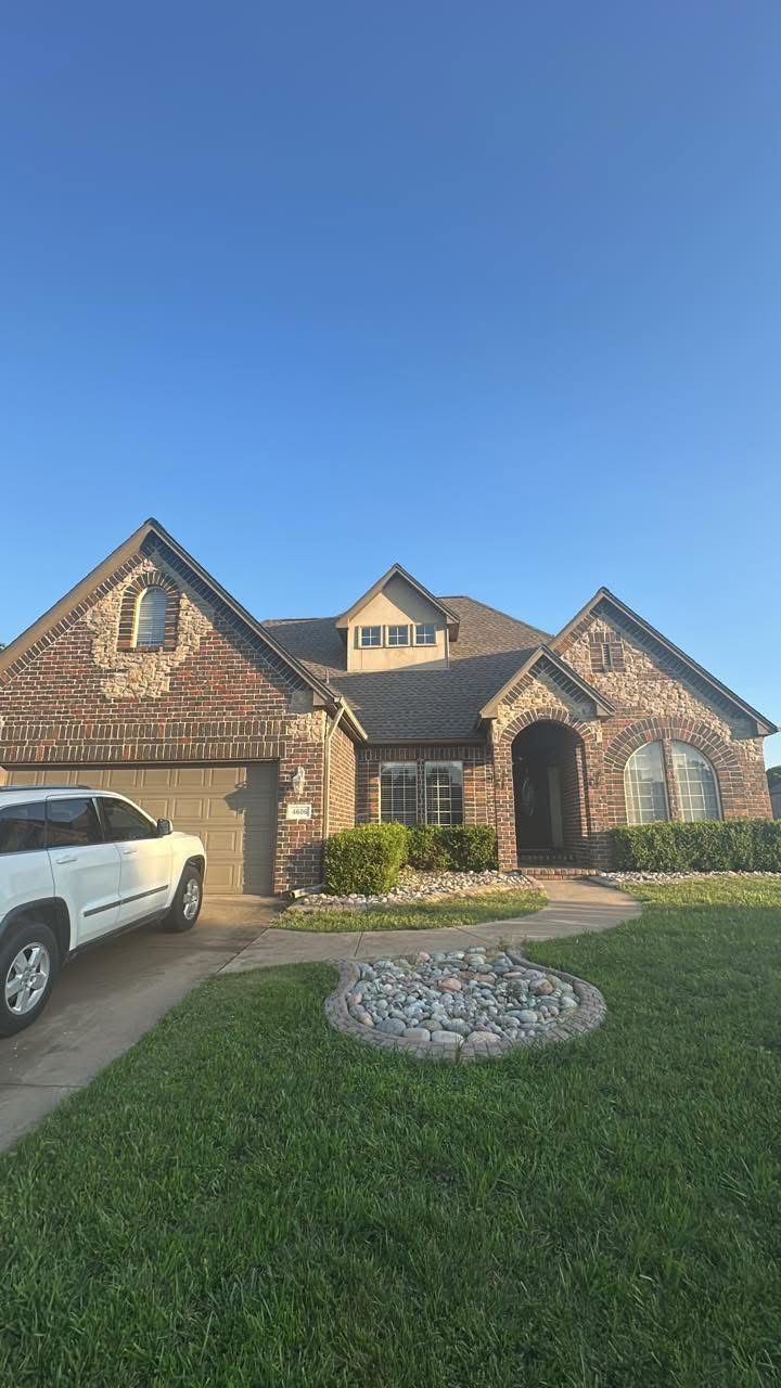 Brick house with a gabled roof, stone walkway, and parked white SUV on a grassy lawn under a clear blue sky