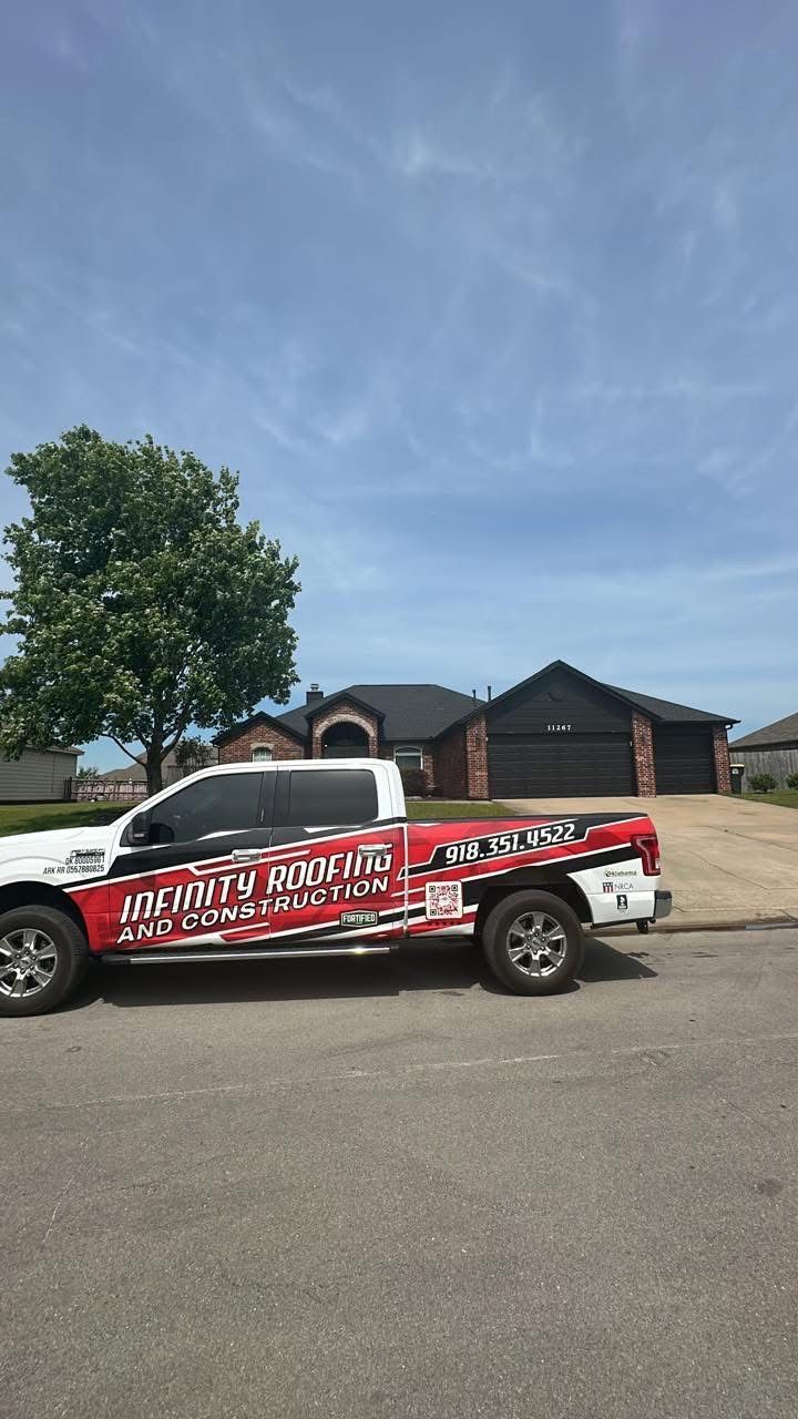 White pickup truck with red graphics parked on a sunny street beside a brick house and a tree