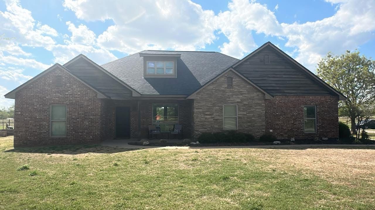 Single-story brick house with a central dormer, front lawn, and cloudy blue sky.