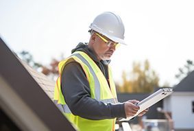 Construction worker in hard hat and safety vest reviewing plans on a rooftop
