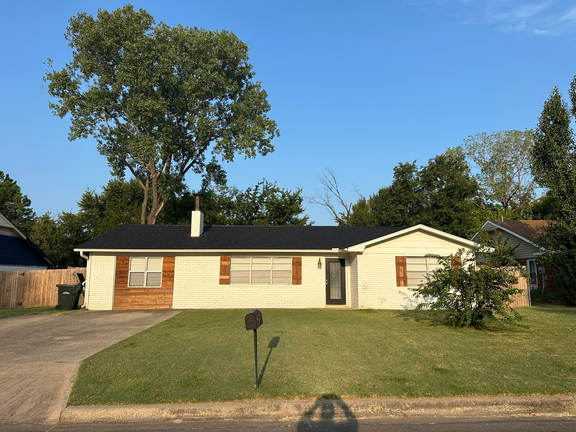 Single-story cream house with brown shutters and a front lawn on a sunny day