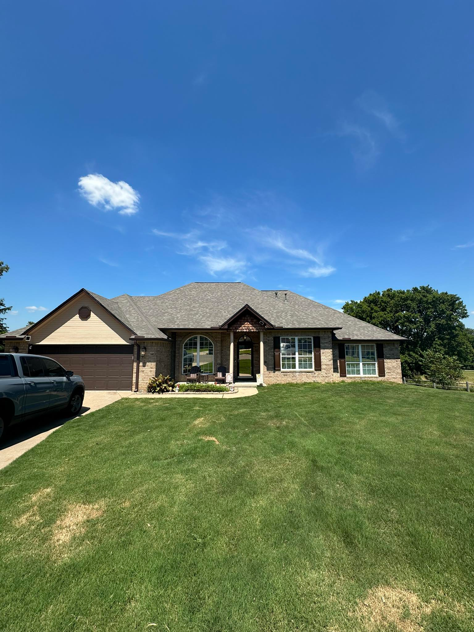 Single-story brick house with a front lawn under a bright blue sky