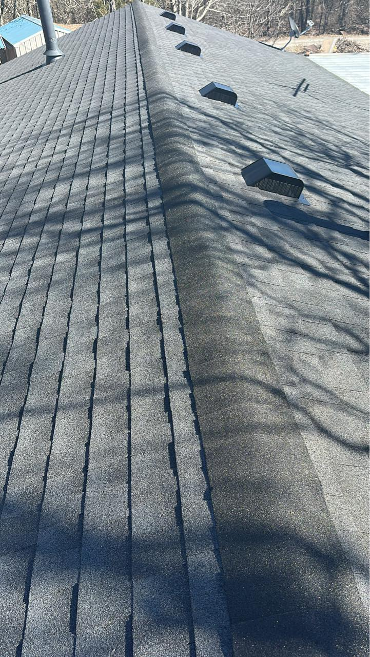 Close-up of a gray shingled roof with tree shadows and a few roof vents.
