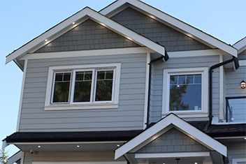 Gray house exterior with white trim and two second-story windows under peaked rooflines