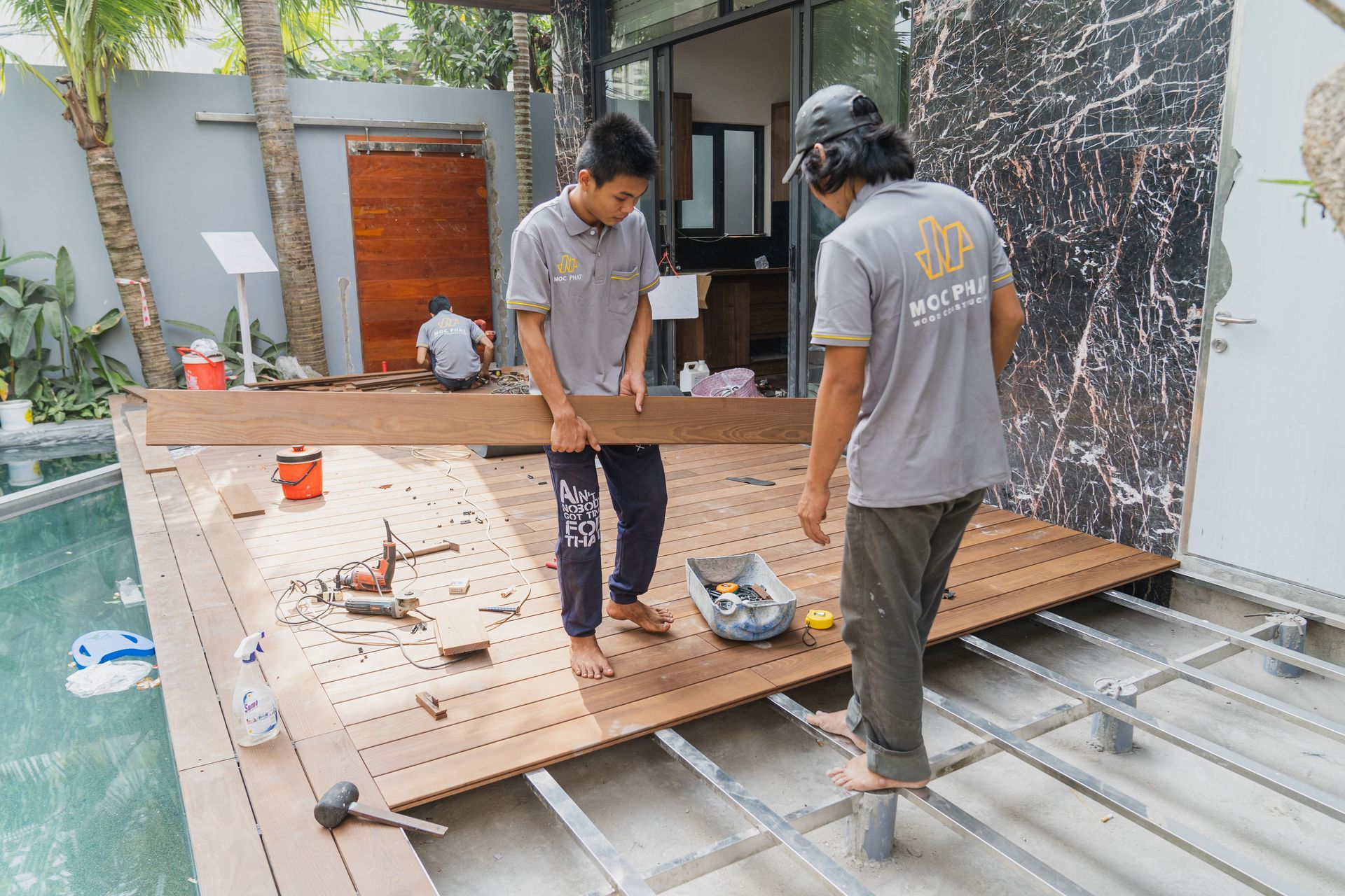 Two workers installing a wooden deck over a steel frame in a courtyard.