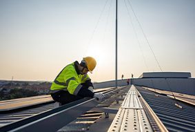 Worker in yellow hard hat and hi-vis jacket inspecting rooftop solar panels at sunset