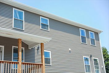 Exterior of a gray two-story house with white trim and a wooden porch under a blue sky