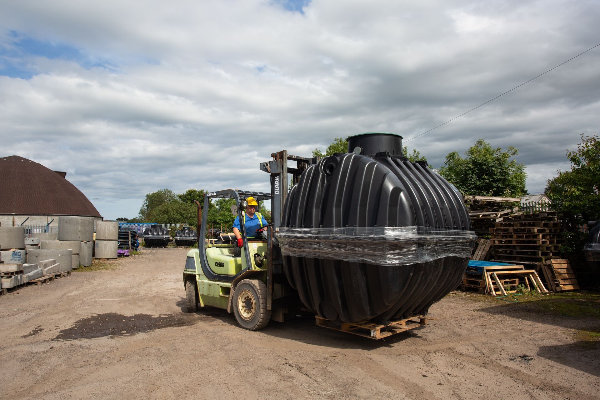 A man is driving a forklift carrying a large black tank.