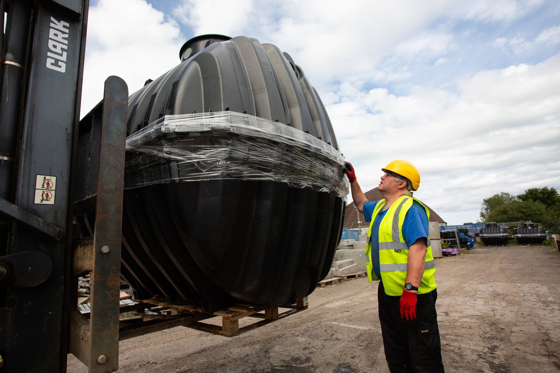 A man in a yellow vest is standing next to a large black object.