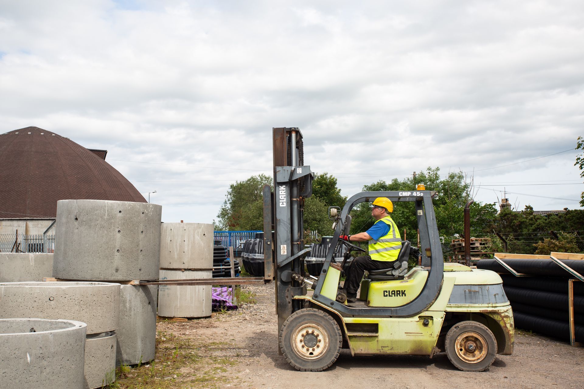A man is driving a forklift on a dirt road.
