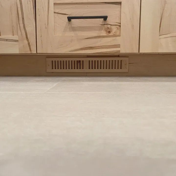 Wooden kitchen cabinets with a center drawer above a beige countertop and vent grille.
