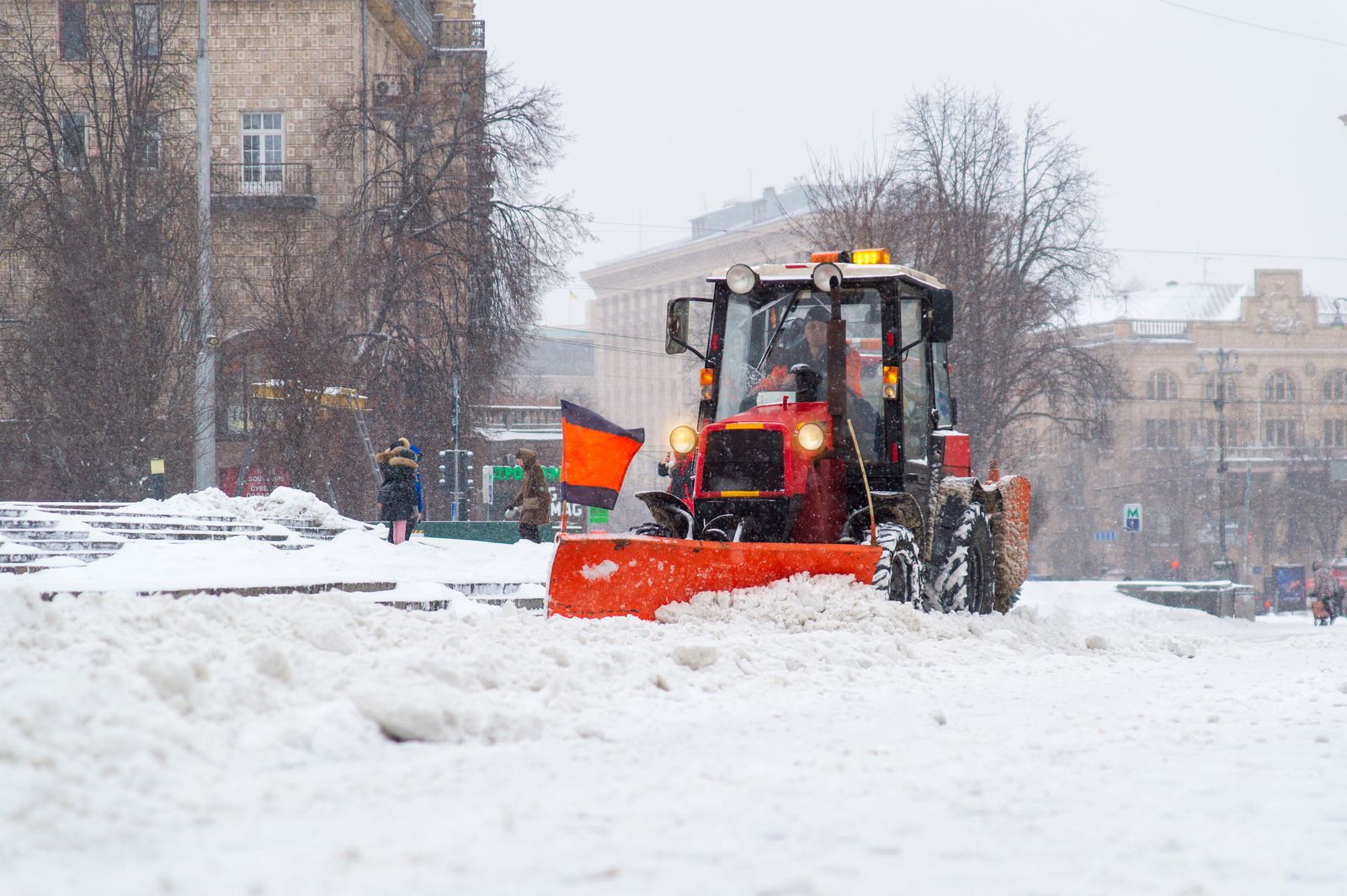 Red snowplow clearing snow from a city street on a snowy day.