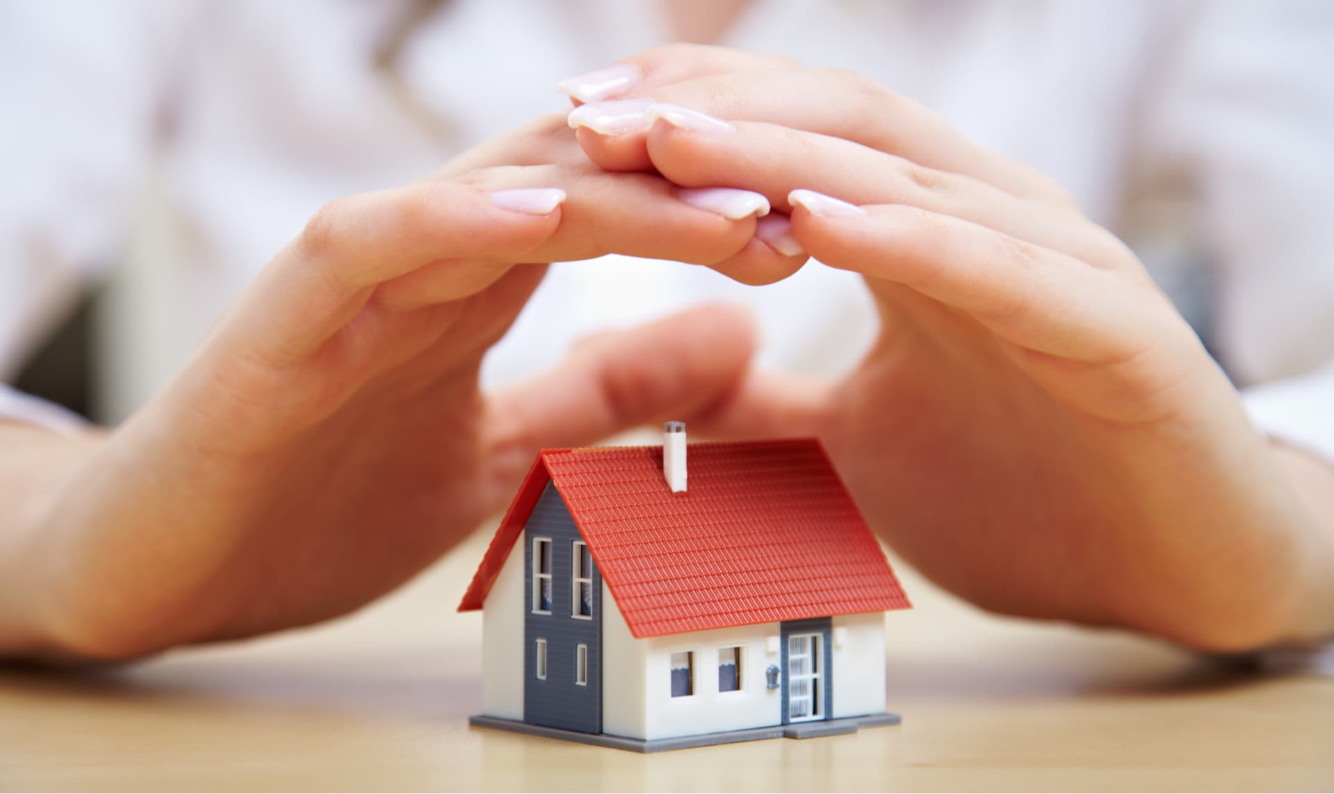 Hands sheltering a small model home, symbolizing homeowners insurance protection after roof storm damage in West Palm Beach