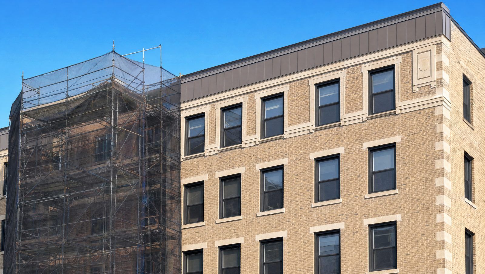 Masonry apartment building facade under restoration with scaffolding and new roof parapet coping