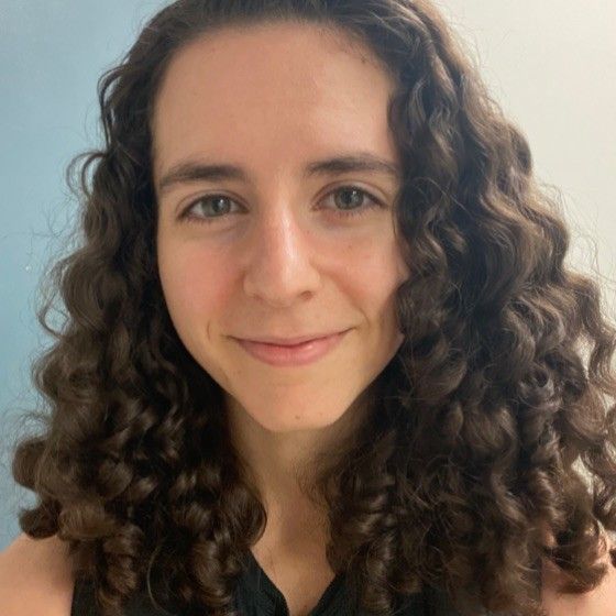Smiling person with curly brown hair against a light background