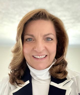 Smiling woman with shoulder-length brown hair, wearing a white turtleneck and navy blazer.