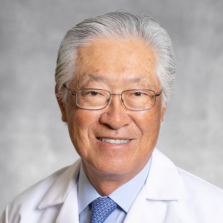 Smiling man in a white coat and glasses against a gray background