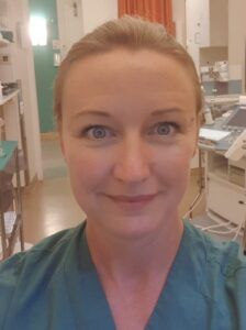 Person in teal scrubs taking a selfie in a medical clinic hallway.