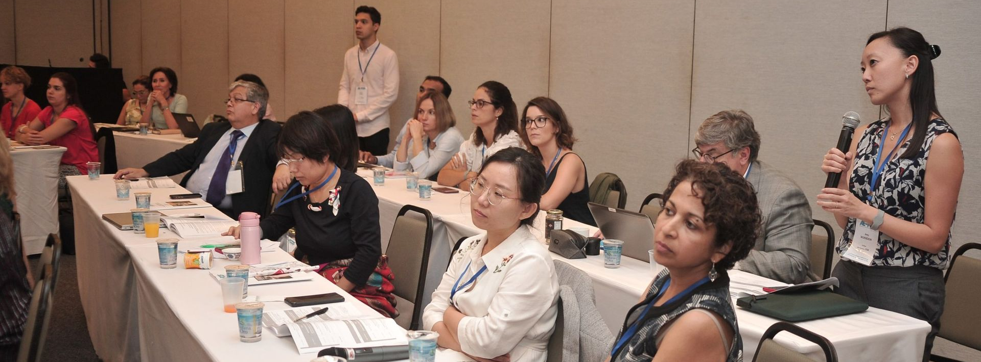 People seated at a long table in a conference room, listening during a meeting