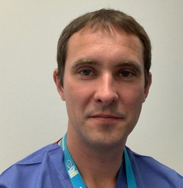 Portrait of a man in blue scrubs and a teal lanyard against a plain wall
