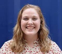 Smiling woman with wavy blonde hair in a floral blouse against a blue background