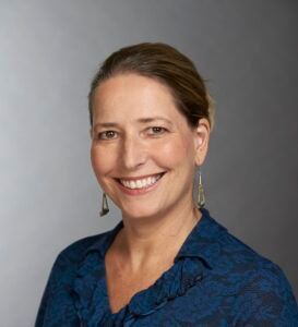 Smiling woman in a blue patterned blouse against a gray background