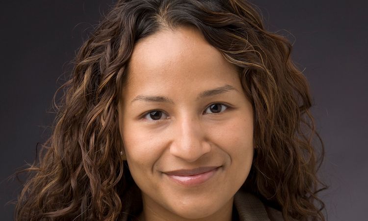 Smiling person with curly hair against a gray background