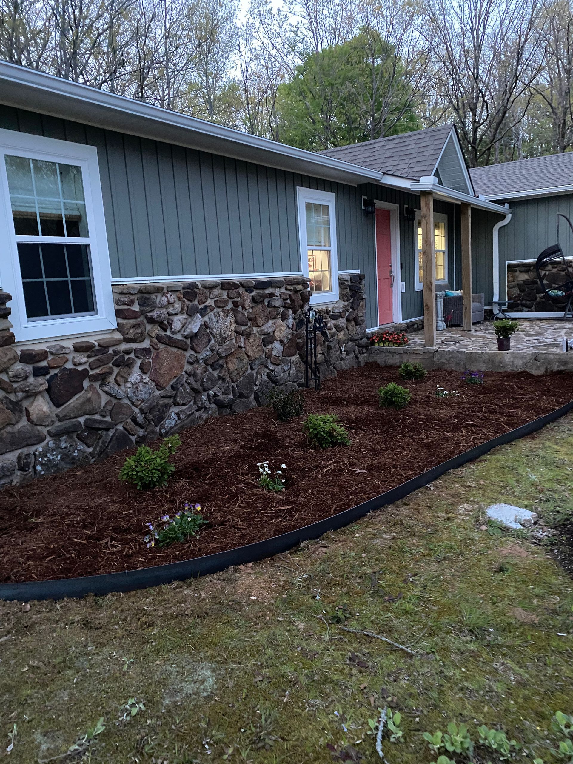 a house with a stone wall and a beautifully maintain garden in front of it.