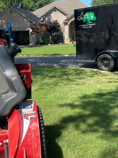 a red lawn mower is parked next to a black trailer with a tree on it .