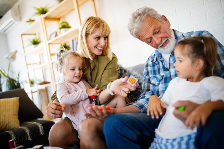 Family sitting together on a couch, sharing a toy in a bright living room.