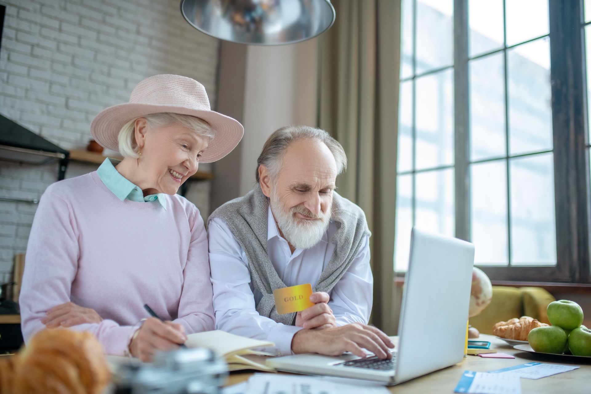 Two people at a table smiling and looking at a laptop in a bright kitchen