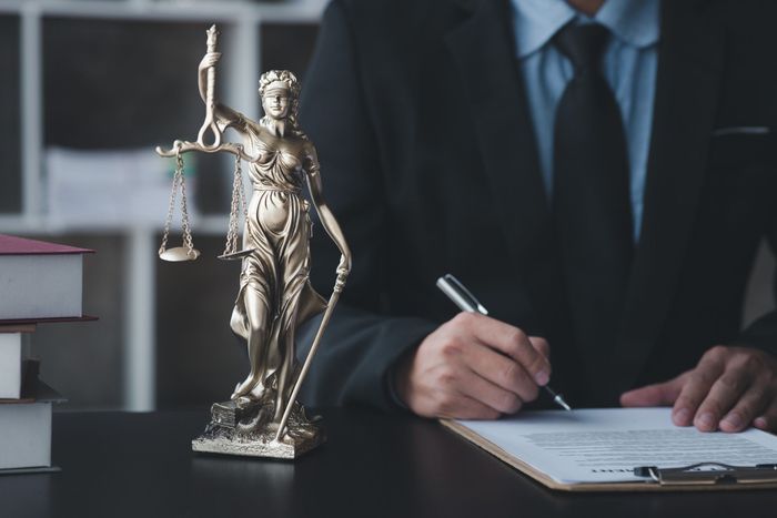 A man is signing a document in front of a statue of justice.
