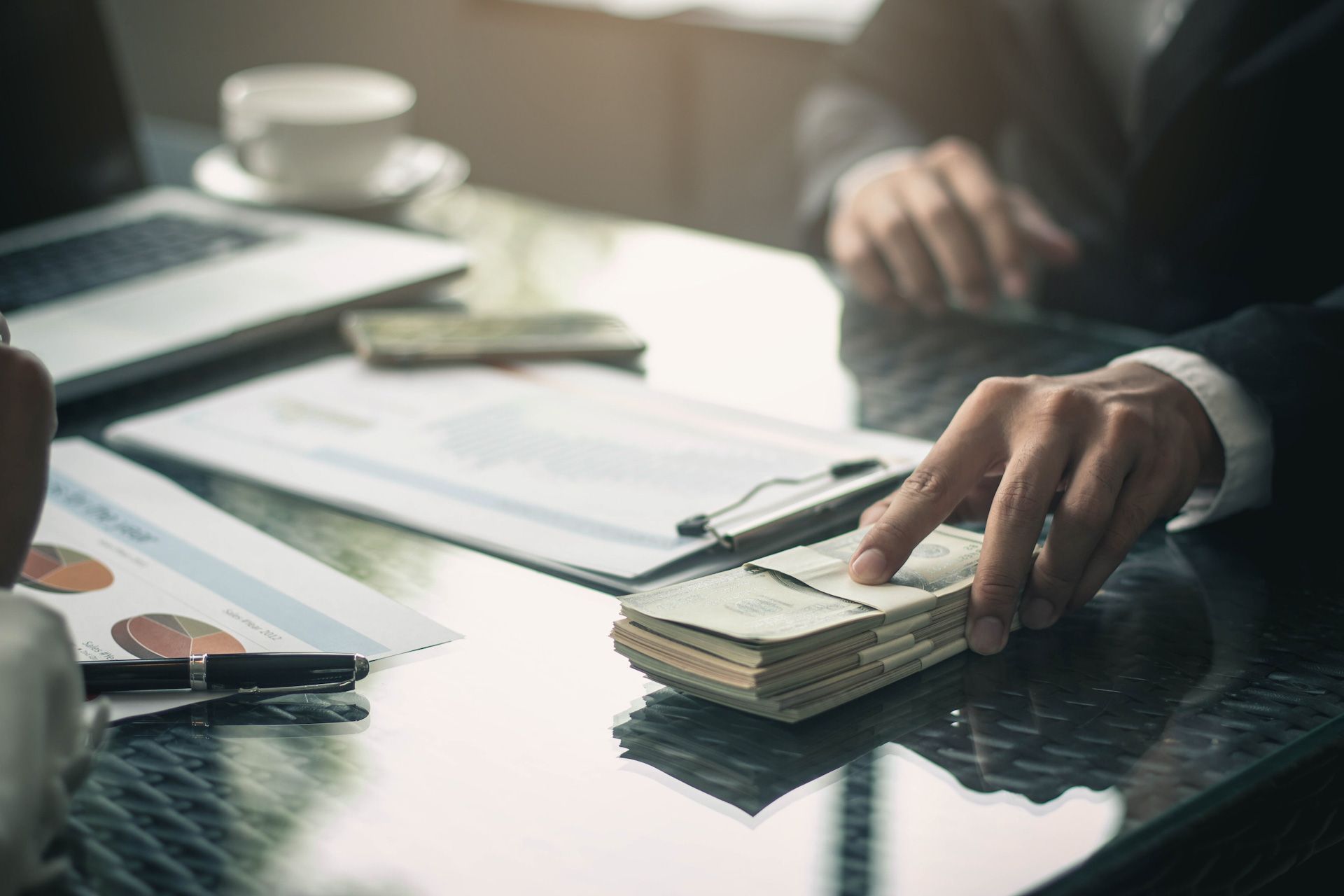 A man is sitting at a desk holding a stack of money and using a calculator.