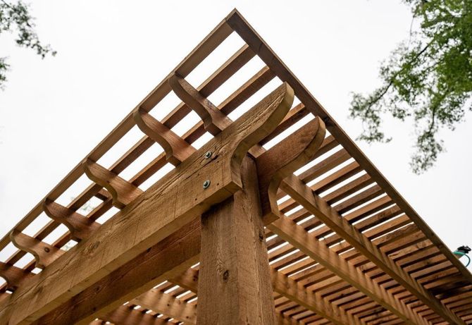Wooden pergola frame viewed from below against a cloudy sky and trees