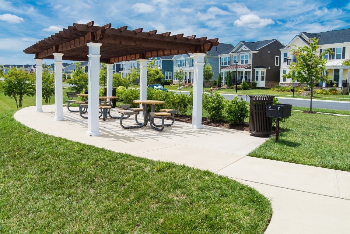 Outdoor picnic shelter with tables beside a sidewalk in a grassy neighborhood park