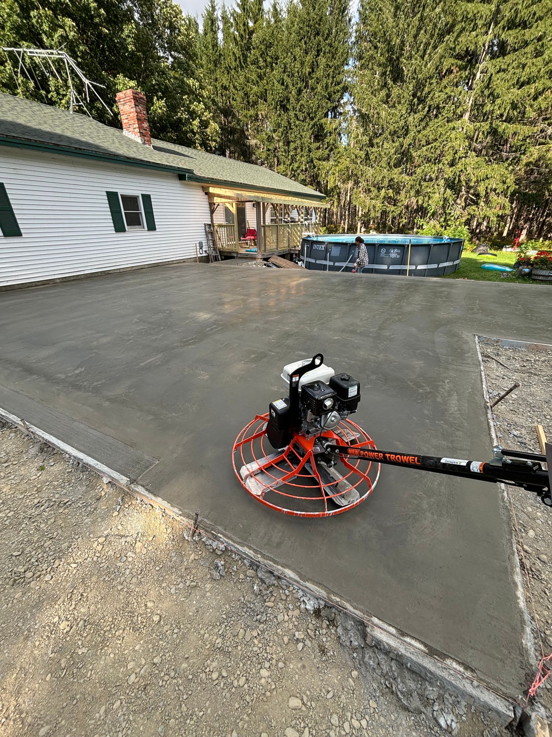 A concrete finisher is being used to finish a driveway in front of a house.