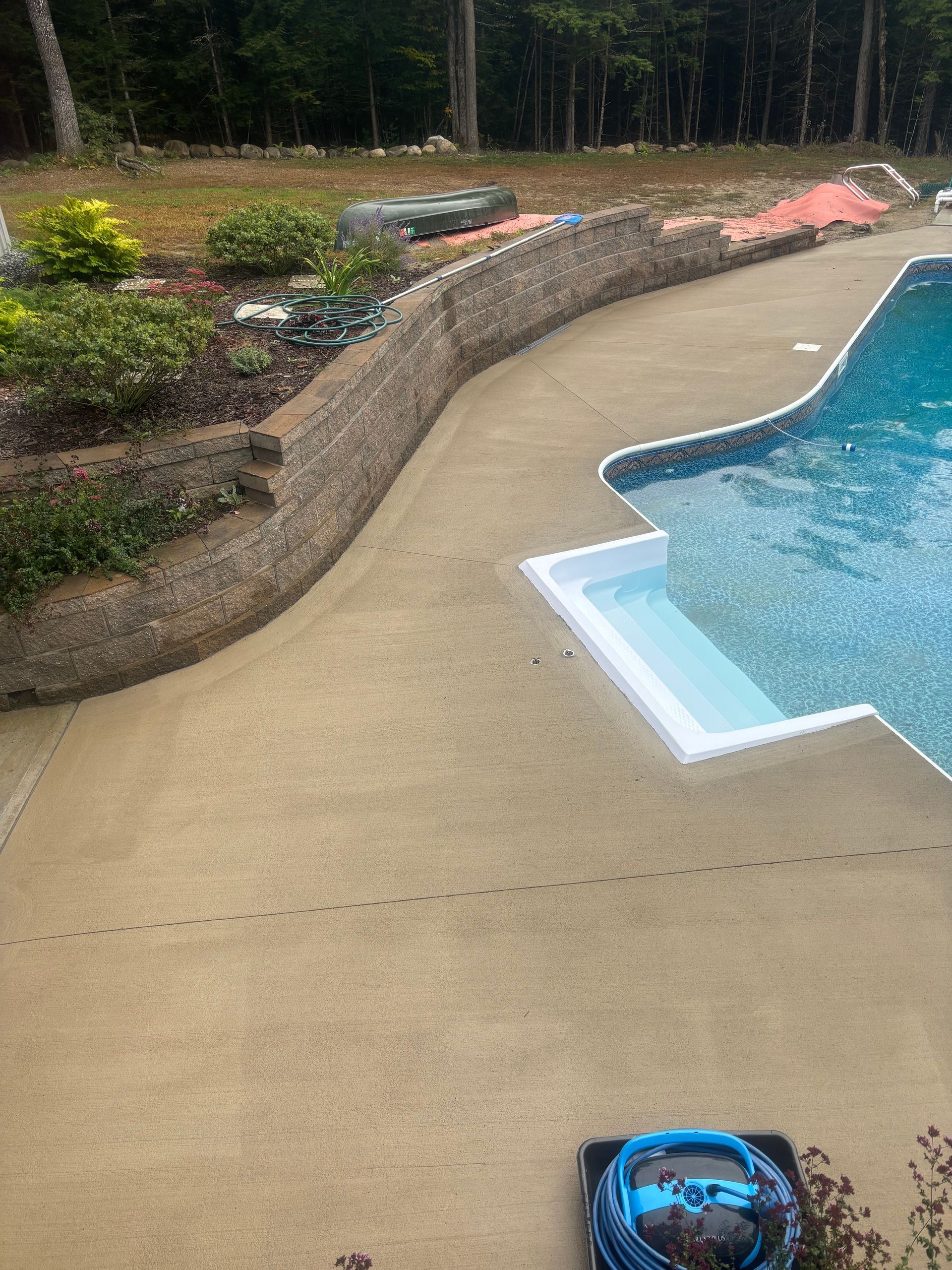 A large swimming pool is surrounded by a concrete patio and a stone wall.