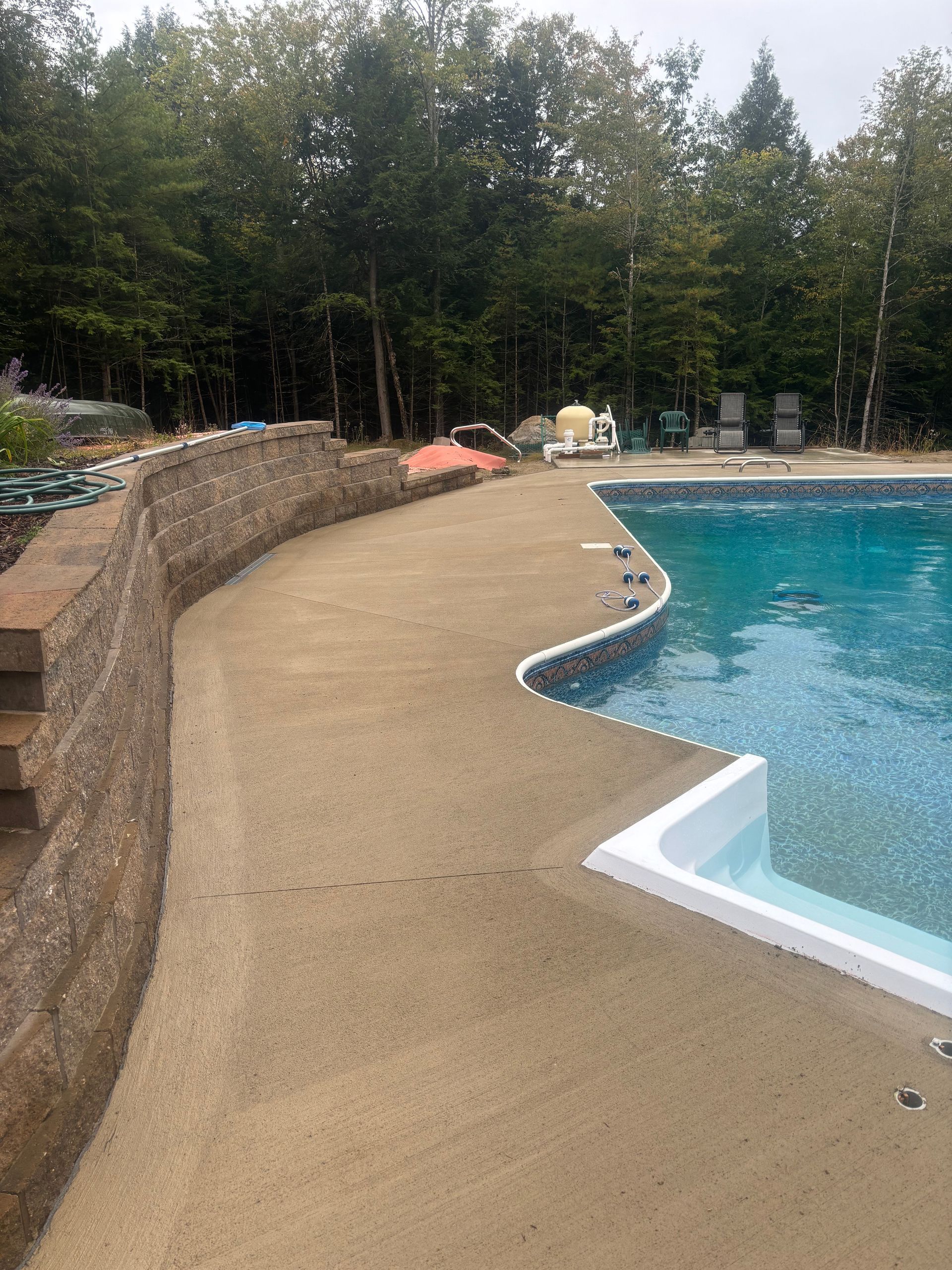 A large swimming pool with a concrete walkway leading to it surrounded by trees.