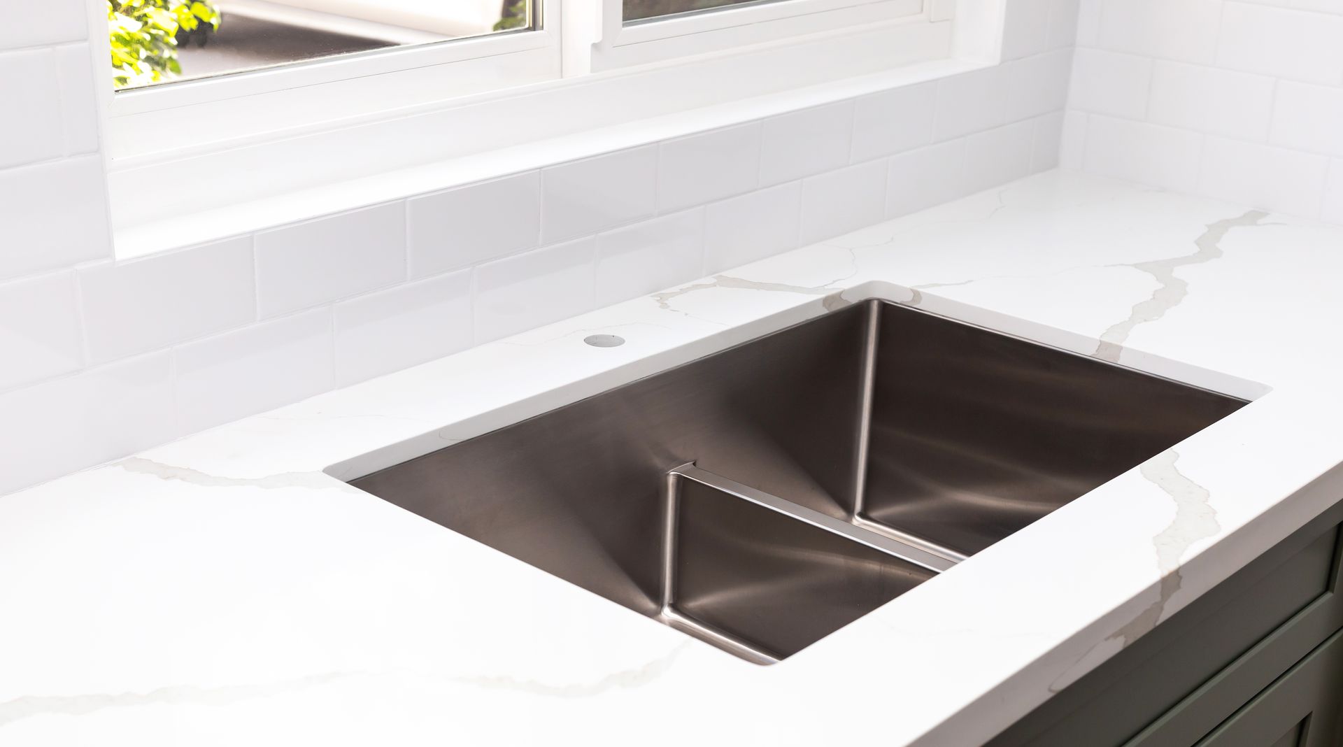 Modern white kitchen countertop with stainless steel undermount sink beneath a window
