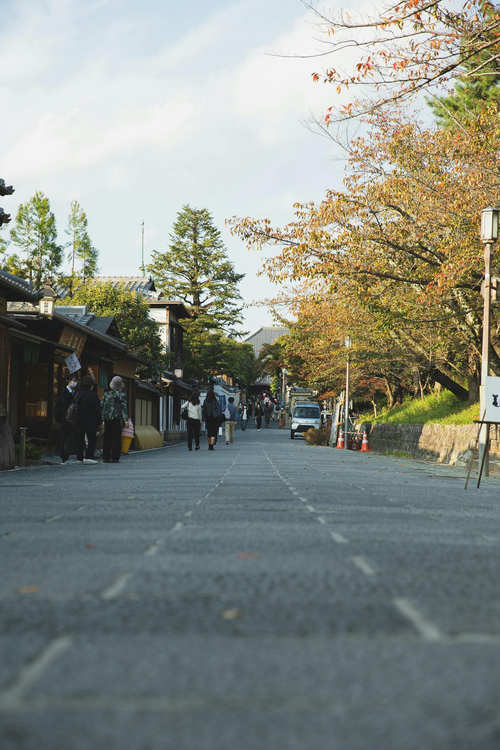 Cobblestone street lined with buildings and autumn trees; people walk down the middle.