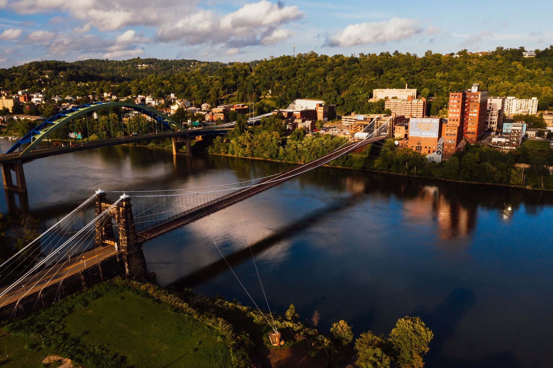 Riverfront cityscape with bridges and buildings under a blue sky and lush greenery.