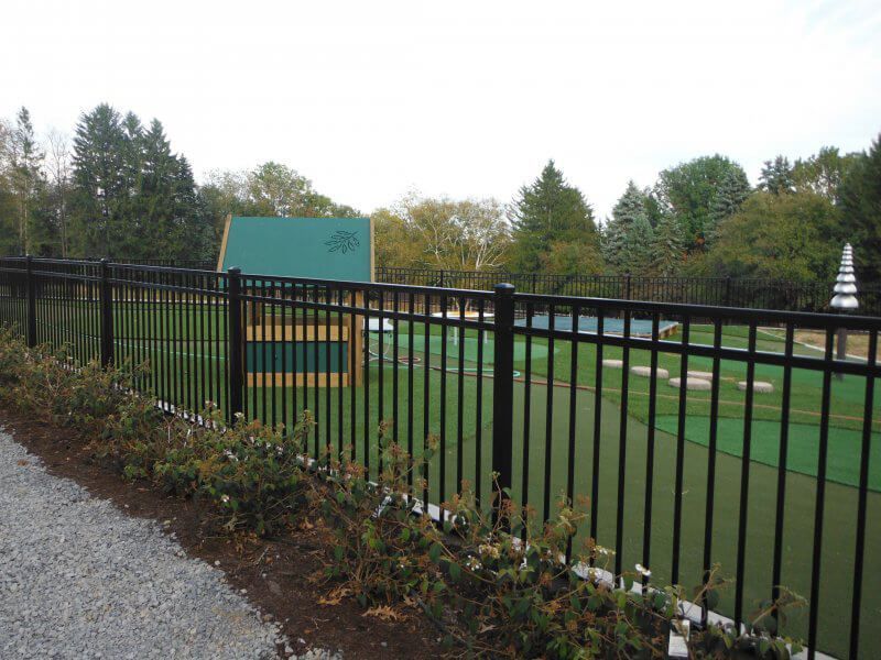 Black fence around a green sports field with a teal sign and trees in the background