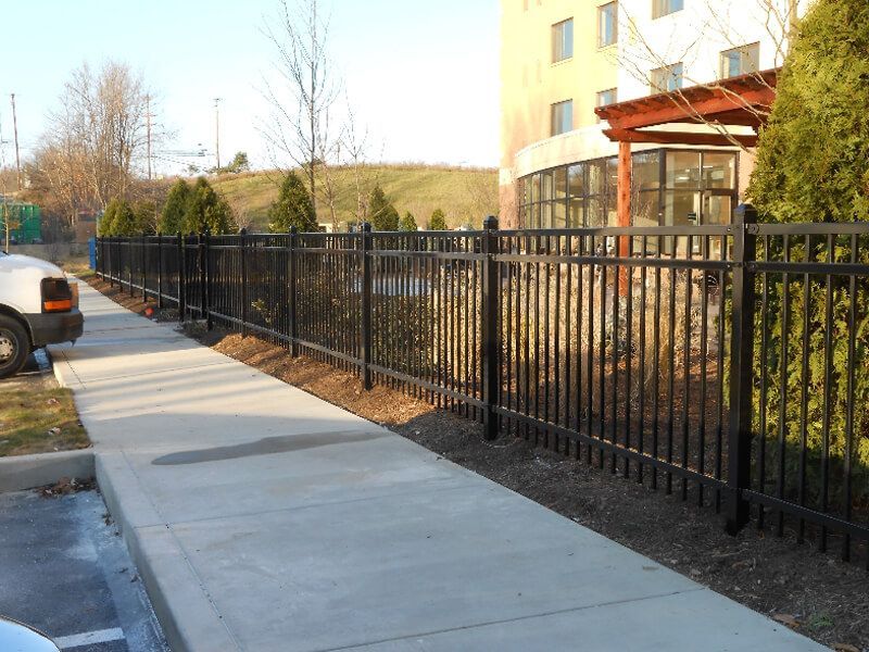 Sidewalk beside a black metal fence and apartment building on a sunny day